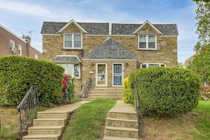 A two-story stone house with a front porch, a small garden, and a pathway leading to the entrance.