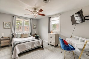 A bedroom with a bed, dresser, desk, chair, ceiling fan, and TV.