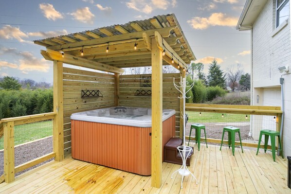 A wooden deck with a hot tub, green stools, and a pergola with string lights.