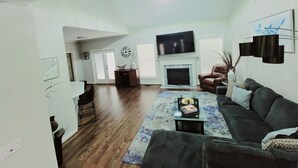 A living room with a fireplace, a television, a sofa, and a coffee table. - Remodeled ranch style home with Firepit conveniently located (Raleigh)