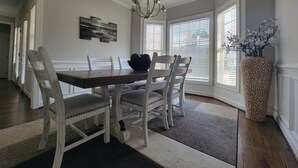 A dining area with a wooden table, white chairs, a chandelier, and a vase with flowers. - Remodeled ranch style home with Firepit conveniently located (Raleigh)
