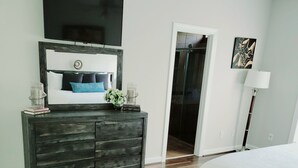 A bedroom with a bed, a dresser, a TV, and a door leading to a bathroom. - Remodeled ranch style home with Firepit conveniently located (Raleigh)
