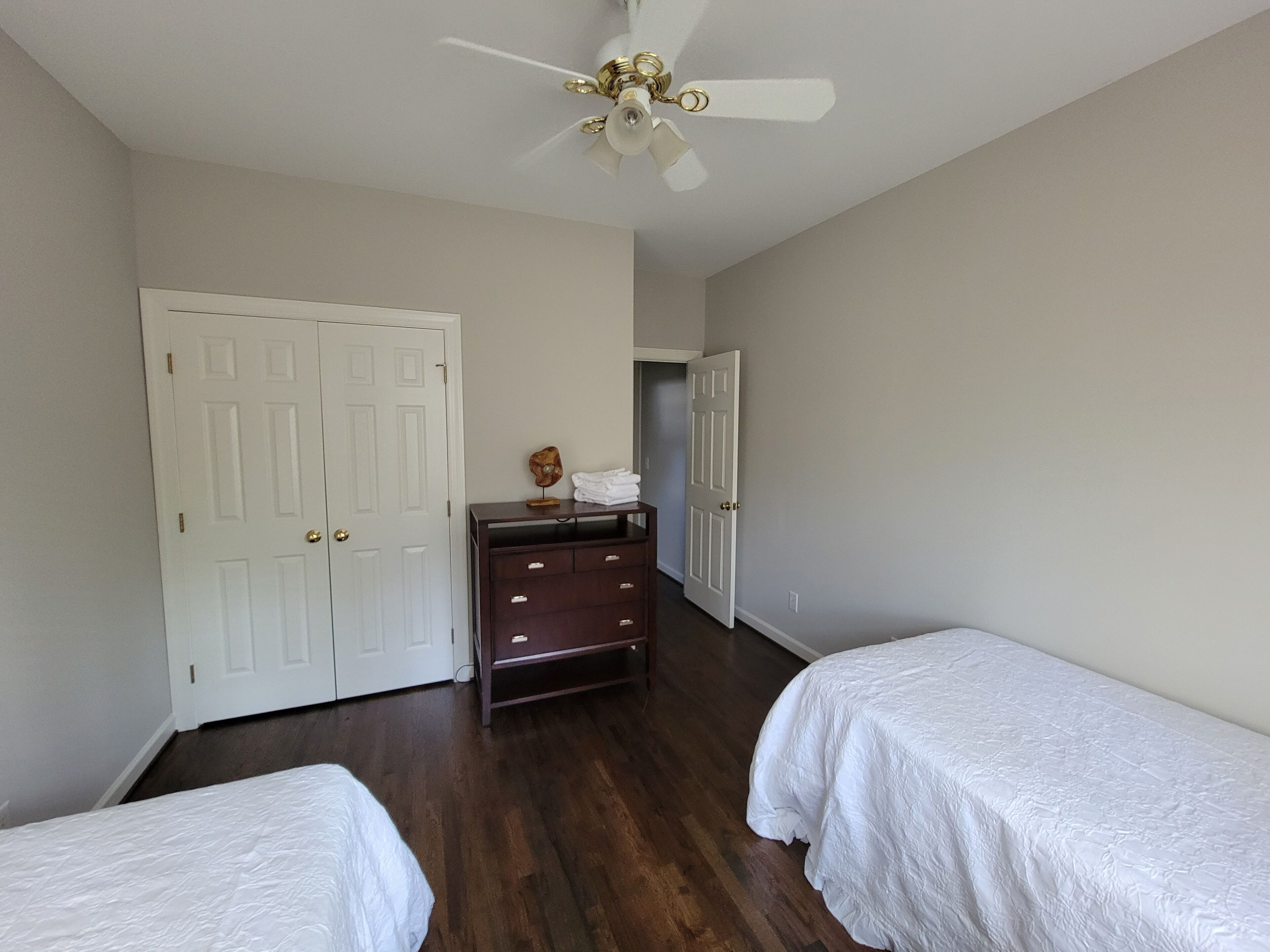A bedroom with two single beds, a dresser, a ceiling fan, and a white door.