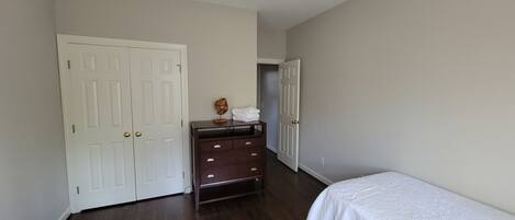 A bedroom with two single beds, a dresser, a ceiling fan, and a white door.