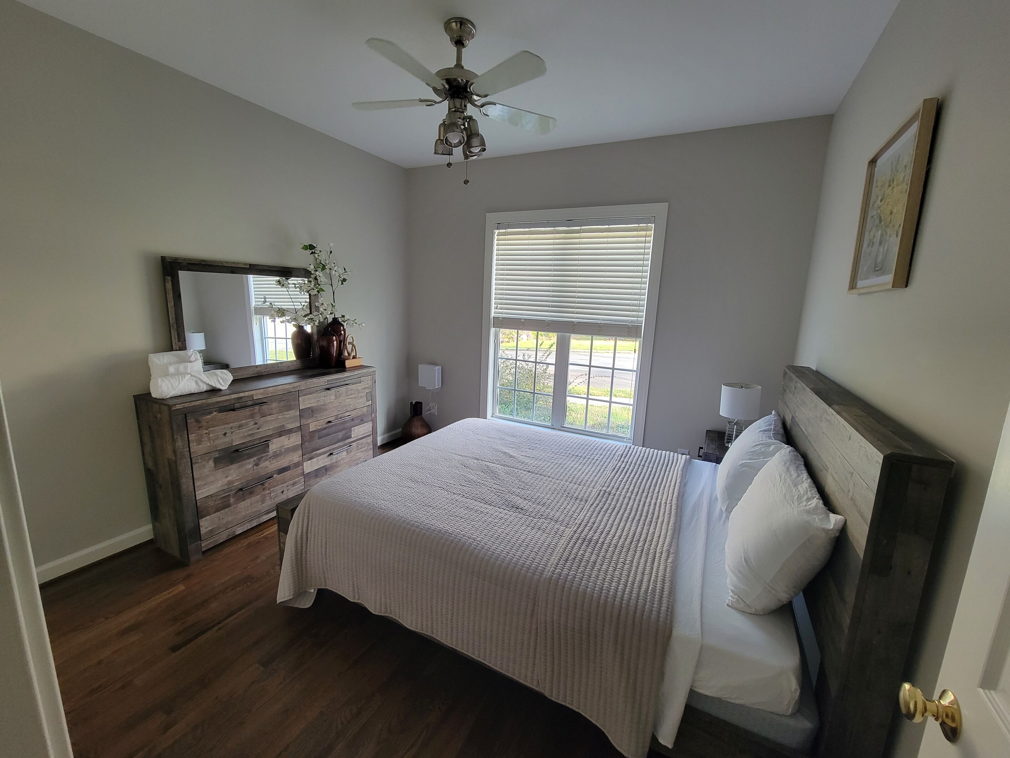 A bedroom with a bed, a dresser, a ceiling fan, and a window with blinds.