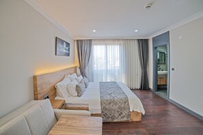 A modern bedroom with a large bed, a bedside table, a sofa, and a bathroom visible through an open door.