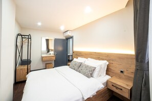 A modern hotel room with a large bed, wooden headboard, bedside tables, a mirror, and a wardrobe.