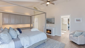 A bedroom with a four-poster bed, a fireplace, a ceiling fan, and a view into another room. - 3809 Sea Foam Oasis - One Block to Miles of Beach (Monterey)