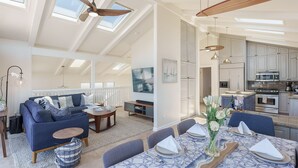 A spacious living area with a high ceiling, skylights, a dining area with a table set for four, and a kitchen with modern appliances. - 3809 Sea Foam Oasis - One Block to Miles of Beach (Monterey)