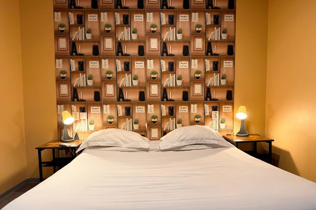 A neatly made bed with a headboard featuring a repeating pattern of books and potted plants.