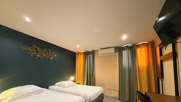 A hotel room with two beds, a desk, a chair, a flat-screen TV, and an air conditioning unit. - Hotel Le Beausejour (Marseille)