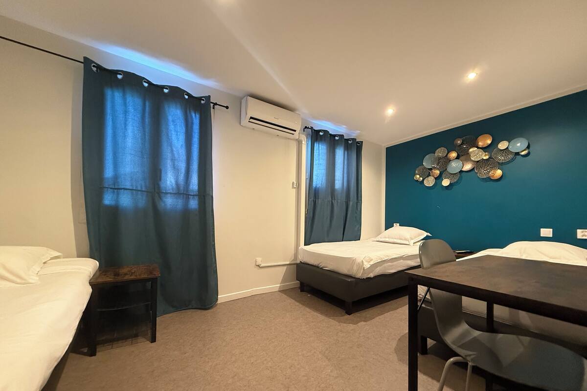 A room with two beds, a desk, and a chair. There is an air conditioning unit on the wall and a wall decoration above the desk.