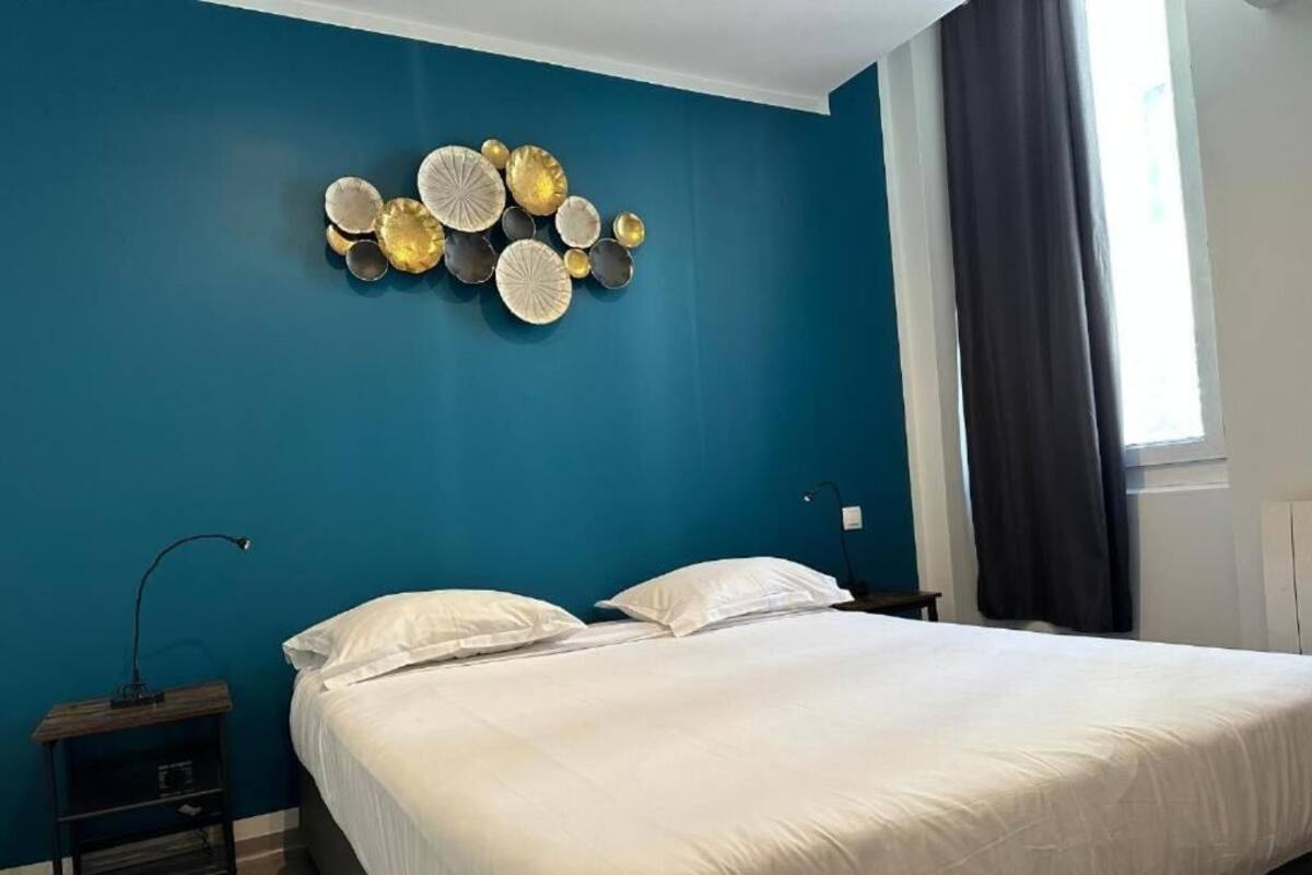 A bedroom with a large bed, a nightstand, a wall-mounted decorative plate arrangement, and a window with curtains.