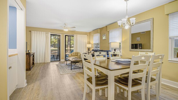 A dining area with a wooden table and white chairs, a ceiling fan, and a chandelier. - PP 200-2 Golfers Paradise in Pawleys Plantation (Pawleys Island)