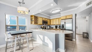A modern kitchen with a large island, stainless steel appliances, and a view of the city. - Emerald Towers 1007 * Beach Chair Set Included * Salt Water Vacations (Fort Walton Beach)