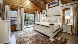 A bedroom with a wooden ceiling, a large bed, a nightstand, and a view of the outdoors. - New and modern cabin with luxury shower room and hot tub (Broken Bow)