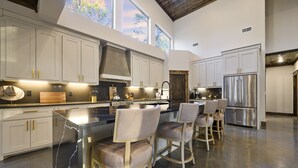 A spacious kitchen with white cabinets, stainless steel appliances, and a large island with bar stools. - New and modern cabin with luxury shower room and hot tub (Broken Bow)