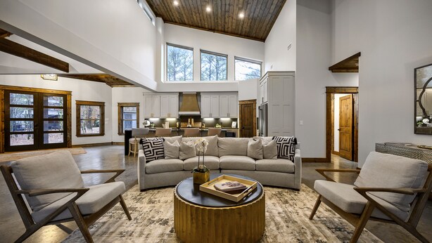 A spacious living room with a large L-shaped sofa, two armchairs, and a round coffee table. The room features a high ceiling with exposed beams, large windows, and a view of the outdoors. - New and modern cabin with luxury shower room and hot tub (Broken Bow)