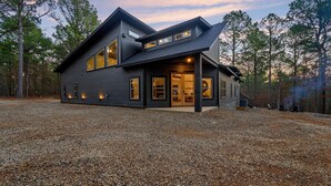 A modern two-story house with a gravel driveway, large windows, and a covered porch area. - New and modern cabin with luxury shower room and hot tub (Broken Bow)
