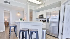 A modern kitchen with white cabinets, stainless steel appliances, and a central island with stools. - Gulf front end unit w/ wraparound balcony, Sunset ocean views, 3BR 3BA! (Panama City Beach)