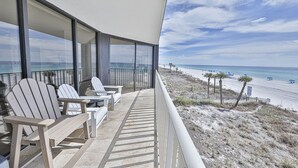 En balkon med Adirondack-stole med udsigt over en strand med palmer og en klar himmel.