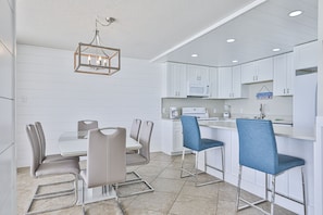 A modern kitchen with white cabinetry, a central island with bar stools, and a chandelier.