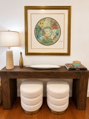 A wooden console table with a framed artwork, a lamp, a vase, a plate, and a book titled 'VOGUE'.