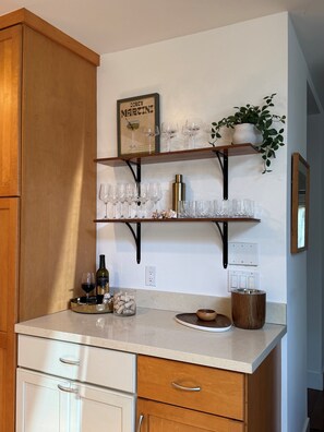 A kitchen with wooden cabinets, a countertop with wine glasses, a bottle of wine, and a potted plant.
