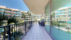 A balcony with a table and chairs, overlooking a pool and a building with multiple balconies.