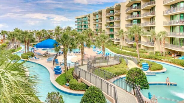 A resort with multiple swimming pools, palm trees, and a large blue tent.