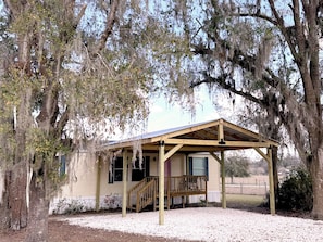 A small, single-story building with a porch and a covered area, surrounded by trees with Spanish moss. - 3BR Cottage with Goats, Covered Patio & Grill, Near Fishhawk (Lithia)