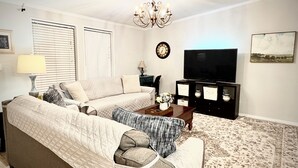 A living room with a sofa, a coffee table, a TV, and a clock on the wall. - Relaxing Cottage Near Fishhawk (Lithia)