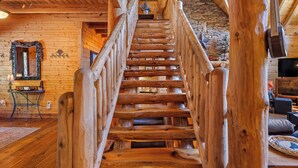 Un escalier en bois avec une rampe, menant à un mur de pierre et à une cheminée.