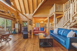 A log cabin interior with a wooden floor, leather sofas, a dining area, and a staircase.
