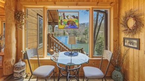 L’intérieur d’un chalet en bois, avec une table et des chaises en verre, un tableau et une vue sur un lac.