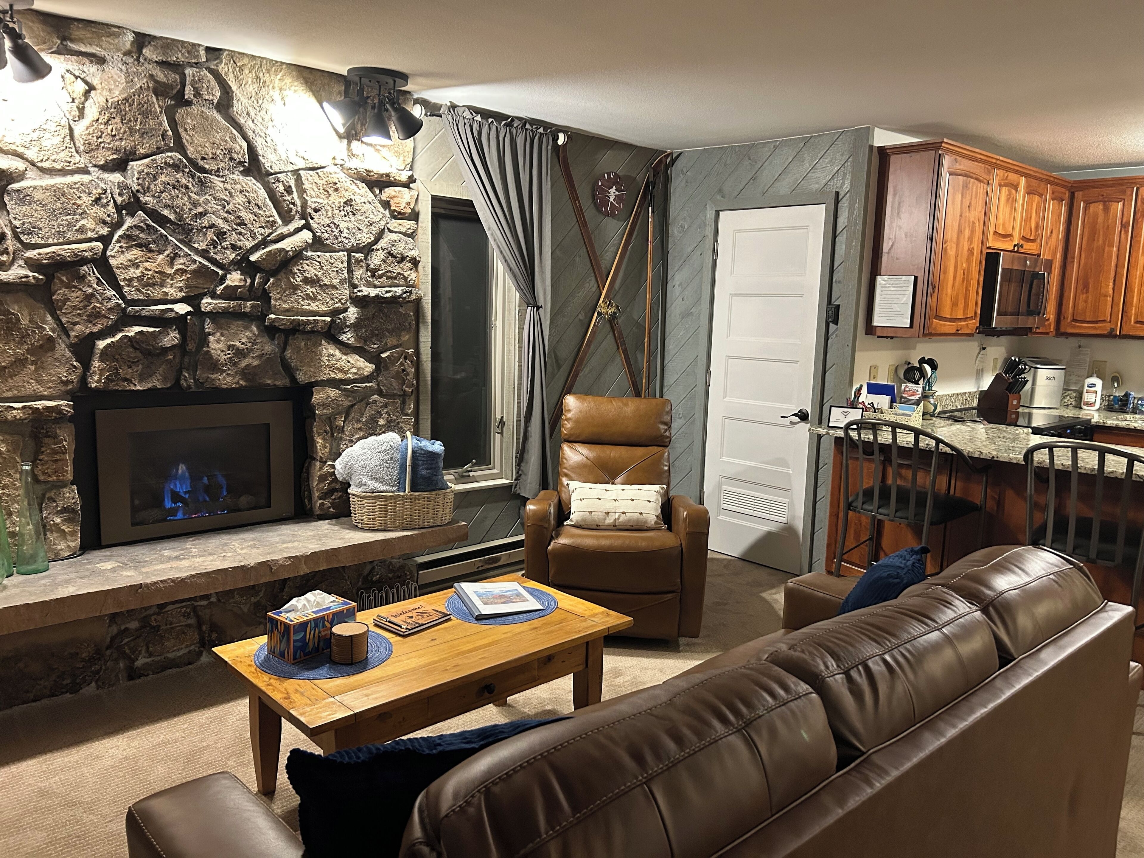 A cozy living room with a stone fireplace, leather armchair, and a wooden coffee table.