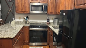 Una cocina con armarios de madera, un microondas de acero inoxidable, un refrigerador negro y una encimera de granito.