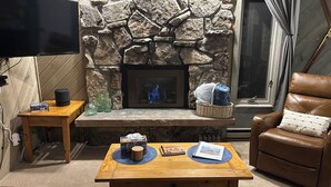 Una sala de estar acogedora con chimenea de piedra, un sillón de cuero y un televisor de pantalla plana montado en la pared.