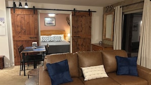 Una habitación acogedora con un sofá de cuero marrón, una mesa de comedor con sillas, una cama con cabecera de madera y un espejo grande.