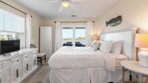 A bedroom with a bed, a television, a dresser, a ceiling fan, and a view of the sea. - Eastern Lake Home + Dock - Walk to Beach + Bikes (Santa Rosa Beach)