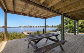 Une terrasse en bois avec une table de pique-nique, donnant sur un lac, avec des maisons en arrière-plan.