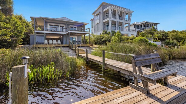 A waterfront property with a wooden dock, a covered seating area, and a multi-story building with balconies. - Eastern Lake Home + Dock - Walk to Beach + Bikes (Santa Rosa Beach)
