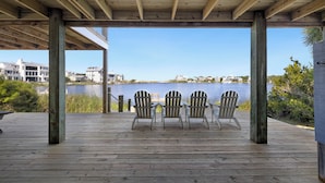 A wooden deck with Adirondack chairs overlooking a lake, with buildings in the background. - Eastern Lake Home + Dock - Walk to Beach + Bikes (Santa Rosa Beach)