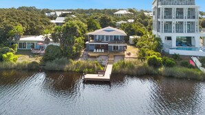 A multi-story house with a dock extending into a body of water, surrounded by lush greenery. - Eastern Lake Home + Dock - Walk to Beach + Bikes (Santa Rosa Beach)