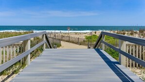 Un paseo marítimo de madera que lleva a una playa con vista despejada al océano.