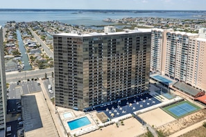 Un hotel moderno con numerosi piani, una piscina, campi da tennis e vista sulla città e sul mare circostanti.