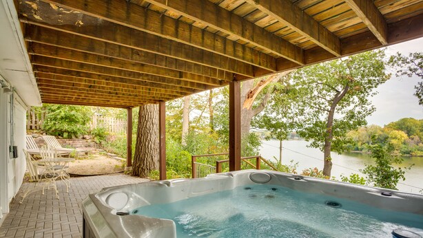 Ein Whirlpool unter einer Holzpergola mit Blick auf einen See und Bäume.