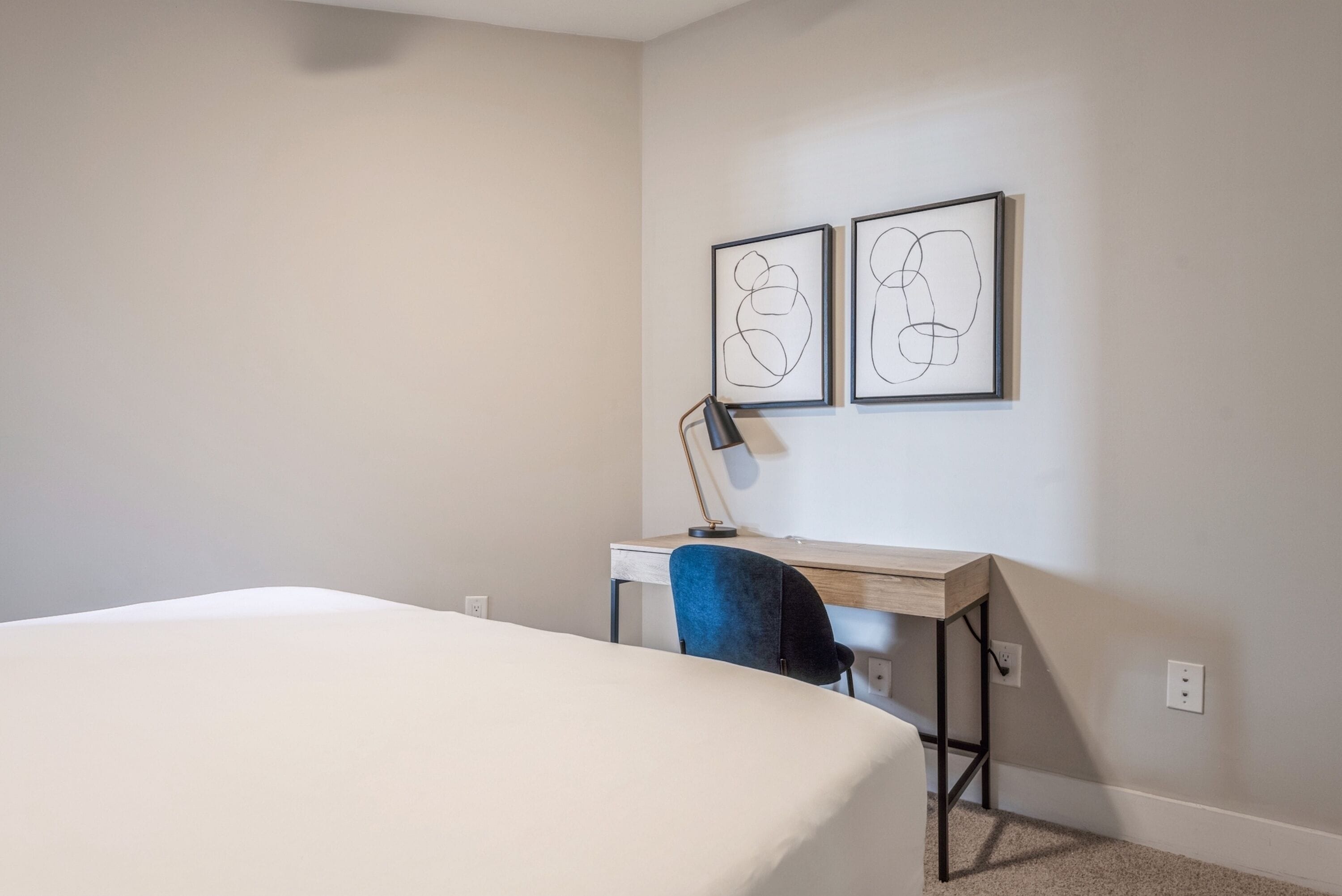 Un dormitorio con cama, un escritorio y dos cuadros abstractos en la pared.