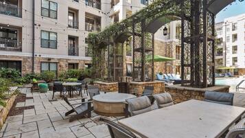 An outdoor patio area with stone flooring, outdoor seating, and a pool in the background.