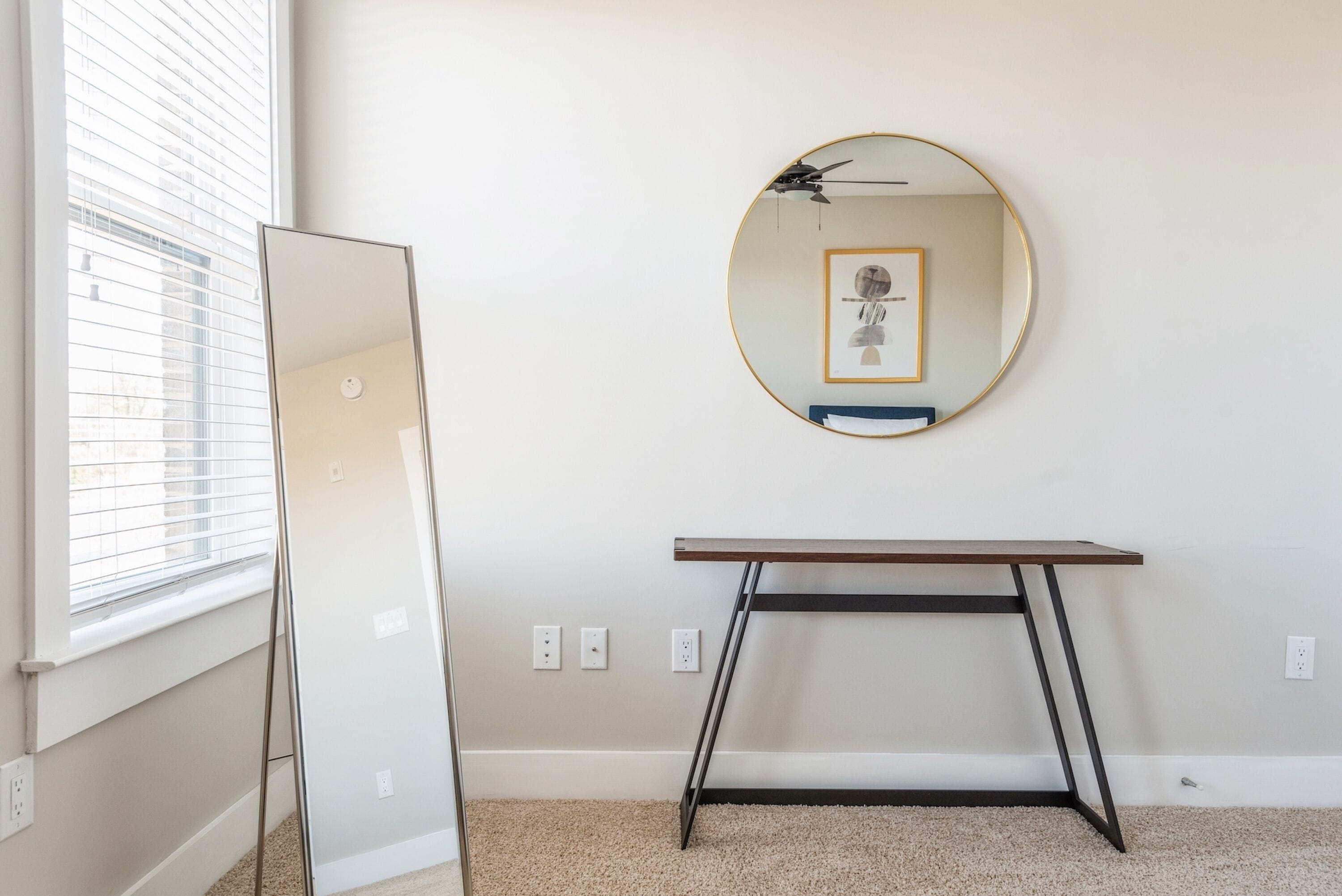 A room with a large mirror, a small table, and a window with blinds.